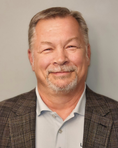 ROB CLABAUGH | OHIO811 Portrait of a smiling middle-aged man with gray hair and a trimmed beard, wearing a blazer and light blue shirt against a neutral gray background.