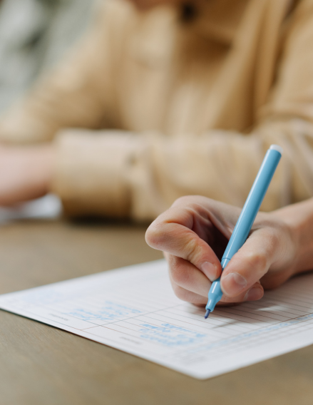 Person writing with a blue pen on a grid notebook on a wooden desk