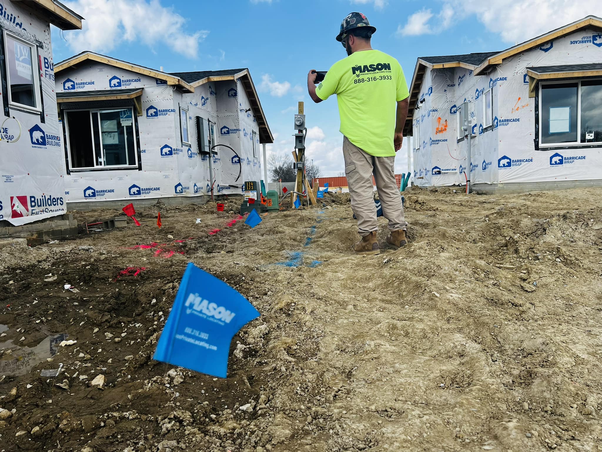 429570887_889441499859051_7333990928592996110_n | OHIO811 Construction worker in a neon shirt photographs a new home under construction with wrapped exterior walls and a blue sky above.